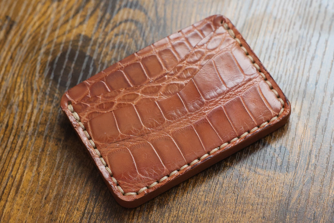 Buckler four-slot card holder in Honey American alligator belly with hand-stitched edges and curved slots, flat lay on a wood table